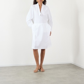 Model wearing Jacquemus white cotton dress with V-neckline, balloon sleeves, and gathered skirt, styled with nude heeled sandals
