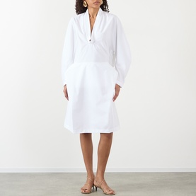 Model wearing Jacquemus white cotton dress with voluminous long sleeves, V-neckline, and structured A-line skirt, styled with nude heeled sandals.