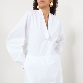 Model wearing Jacquemus white cotton dress with V-neckline and balloon sleeves, styled with gold drop earrings