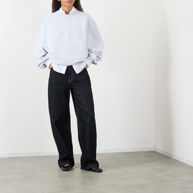 Model wearing Jacquemus grey sweat top in relaxed fit, styled with dark wide-leg jeans and black flat shoes.