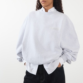 Model wearing Jacquemus grey sweat top with frill mock neck, oversized fit, and small embroidered logo on chest, styled with black trousers
