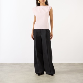Model wearing Jacquemus Light Pink cotton sleeveless top with draped shoulder detail, styled with wide-leg black trousers.