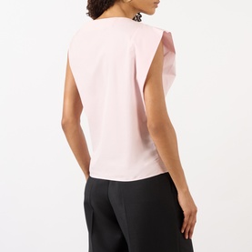 Model wearing Jacquemus light pink cotton top with ruffle cap sleeves, shown from behind, styled with black trousers