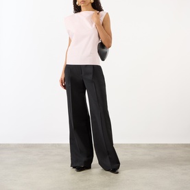 Model wearing Jacquemus light pink cotton sleeveless top with shoulder detail, styled with wide-leg black trousers, carrying a black mini bag.