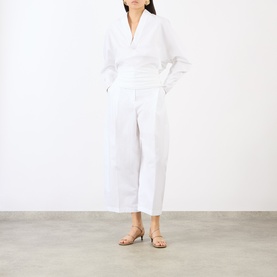 Model wearing Jacquemus white cotton trousers, cropped wide-leg fit, styled with a white wrap top and gold strappy sandals.