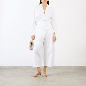 Model wearing Jacquemus white wide-leg cropped cotton trousers, styled with a white blouse, small woven bag, and tan heeled sandals.