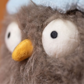 Jellycat brown felted owl plush close-up showing large white eyes, golden beak and fluffy textured fur with pale blue head detail