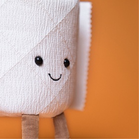 Jellycat Amuseables white toilet roll plush soft toy with smiley face and small legs, against orange background