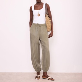Model wearing khaki tapered drawstring trousers, styled with white vest top, woven tote bag and white sandals