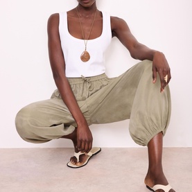 Model wearing sage green harem-style drawstring trousers, styled with white tank top, pendant necklace and strappy flat sandals