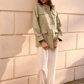 Model wearing sage green oversized utility jacket with chest pockets, styled with white wide-leg trousers