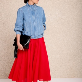 Model carrying black fringed clutch bag, styled with light blue denim jacket and red midi skirt