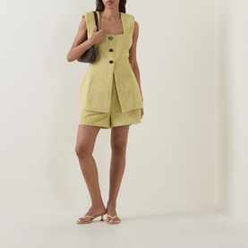 Model wearing Odd Muse Boucl&eacute; Tailored Shorts in chartreuse, styled with matching waistcoat, nude sandals, and dark shoulder bag.