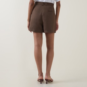 Model wearing Odd Muse Solid Pleated Shorts in mushroom, rear view showing clean hems and jetted pocket, styled with nude heeled mules.