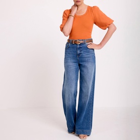 Model wearing orange puff-sleeve knit top with wide-leg blue denim jeans and a tan leather belt.
