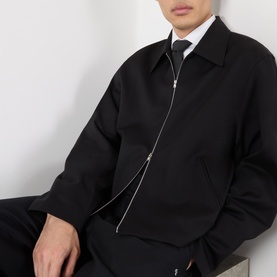 Model wearing Our Legacy black wool casual jacket with asymmetric zip fastening, styled with white shirt and black tie.