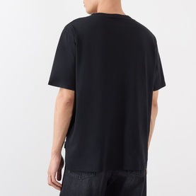Model wearing Our Legacy black cotton T-shirt, rear view, relaxed fit with drop shoulders, styled with dark trousers.