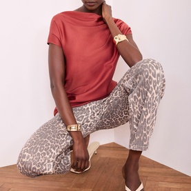 Model wearing grey leopard print trousers with rust red short-sleeve top, gold cuff bracelet, and white flat shoes
