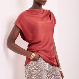 Model wearing a rust red satin-finish short sleeve top with draped neckline, styled with leopard print trousers and gold cuff bracelets.