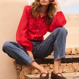 Model wearing Mint Velvet red frill-detail blouse with puff sleeves, styled with blue wide-leg jeans and brown mule sandals.