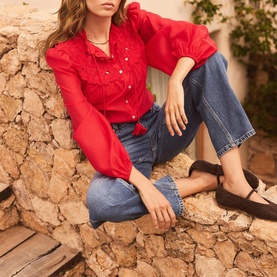 Model wearing Mint Velvet red blouse with puff sleeves and ruffle detail, styled with wide-leg blue jeans and black flat shoes