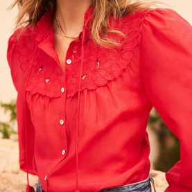 Model wearing Mint Velvet red broderie anglaise frill bib blouse with puff sleeves and button front, styled with gold necklace and jeans.
