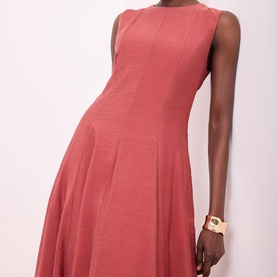 Model wearing Mint Velvet Asymmetric Pleated Dress in red, sleeveless with crew neckline and nipped waist, styled with a gold cuff bracelet.