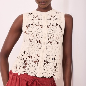 Model wearing Mint Velvet Sparkle Crochet Waistcoat in beige, featuring floral crochet pattern and button front, styled with red shorts.