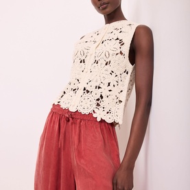 Model wearing Mint Velvet Sparkle Crochet Waistcoat in beige with floral crochet detail, styled with rust-red drawstring shorts.