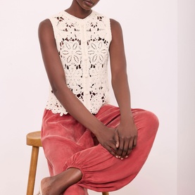 Model wearing Mint Velvet Sparkle Crochet Waistcoat in beige with floral crochet detail and button front, styled with dusty pink velvet trousers.