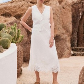 Model wearing Mint Velvet white sleeveless waistcoat top and midi skirt with broderie anglaise hem, styled in a desert setting.