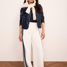 Model wearing white wide-leg trousers with black side stripes, styled with a navy jacket and cream scarf