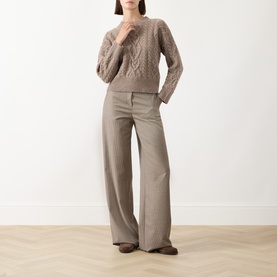 Model wearing taupe cable-knit jumper styled with wide-leg tailored trousers and brown flat shoes