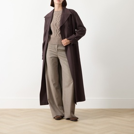 Model wearing a longline dark brown belted wool coat, styled with a cream knit jumper, wide-leg trousers, and flat shoes.