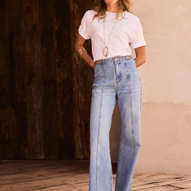Model wearing Mint Velvet blue wide-leg jeans with contrast panel detail, styled with a white cropped tee and long pendant necklace.