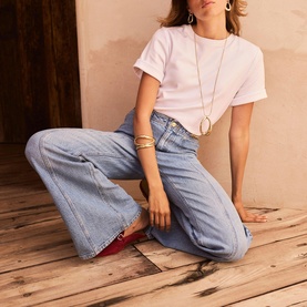 Model wearing Mint Velvet blue wide-leg jeans with a pale pink T-shirt, gold jewellery and red shoes
