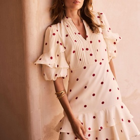 Model wearing Mint Velvet cream dress with red polka dots, ruffle sleeves and V-neckline; styled with gold bangles