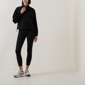 Model wearing Sweaty Betty black zip-neck jacket with black leggings and grey trainers