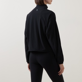 Model wearing Sweaty Betty black jacket, rear view, with matching black leggings. Small logo detail at back neck.