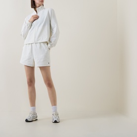 Model wearing Sweaty Betty Lily White jacket with matching white shorts, white ankle socks and grey trainers