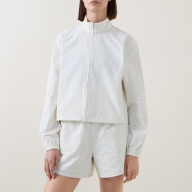Model wearing Sweaty Betty Lily White zip-up jacket with mock neck, styled with matching white shorts.