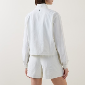 Model wearing Sweaty Betty jacket in Lily White, shown from behind, with matching white shorts. Mock neck collar, long sleeves.