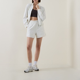Model wearing Sweaty Betty Lily White zip-up jacket with matching shorts, black crop top, and chunky trainers