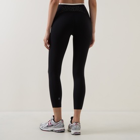 Model wearing Sweaty Betty black leggings with lace-trim waistband, shown from behind, styled with white trainers
