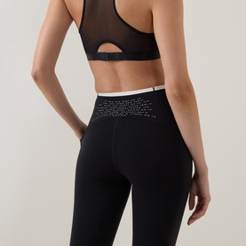 Model wearing Sweaty Betty black leggings with embellished waistband detail, styled with a black mesh sports bra. Rear view.