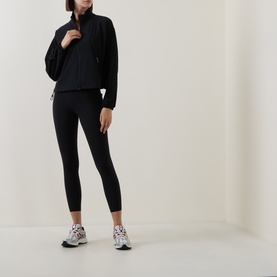 Model wearing Sweaty Betty black leggings styled with a matching black half-zip jacket and white chunky trainers.