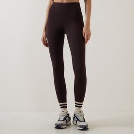 Model wearing Sweaty Betty Espresso Brown leggings with stripe cuffs, styled with white ankle socks and grey trainers.
