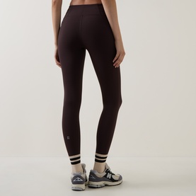 Model wearing Sweaty Betty leggings in Espresso Brown with striped ankle detail, styled with grey trainers, rear view.