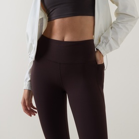 Model wearing Sweaty Betty Espresso Brown leggings with side pockets, styled with a white zip jacket and black sports bra.