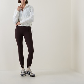 Model wearing Sweaty Betty Espresso Brown leggings, styled with a white zip-up jacket, stripe socks and grey trainers.